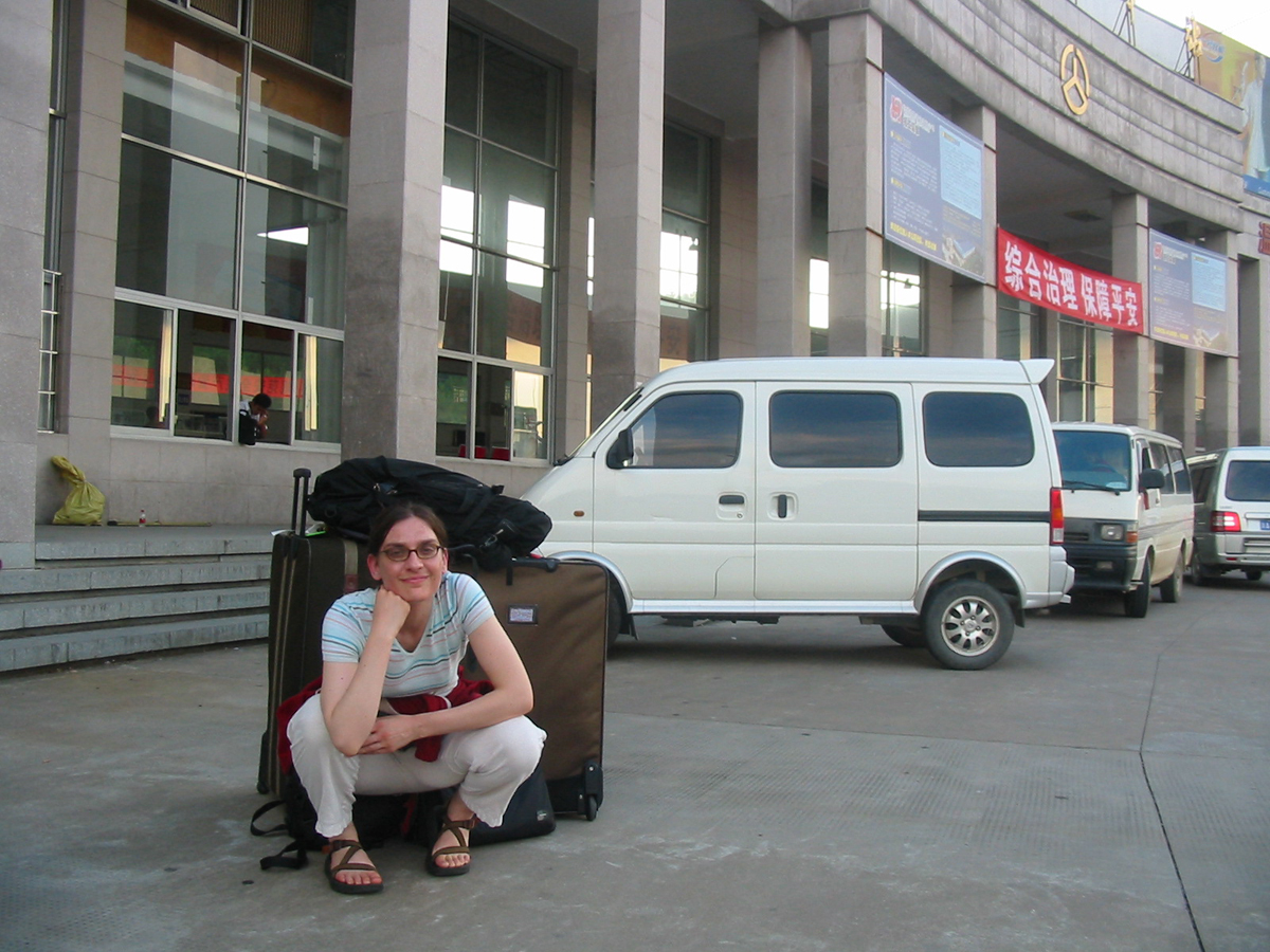 Western woman with luggage by bus station in China